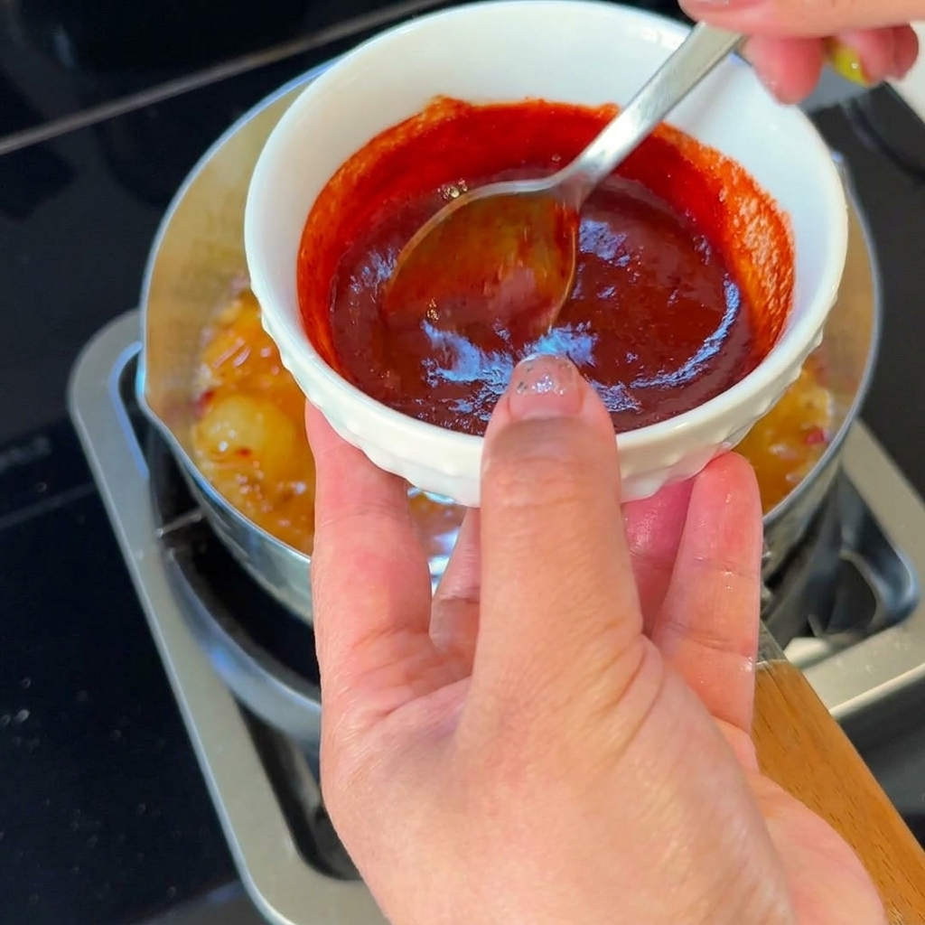 Un cucchiaio che versa una miscela di salsa rossa speziata nello stufato di kimchi in ebollizione.