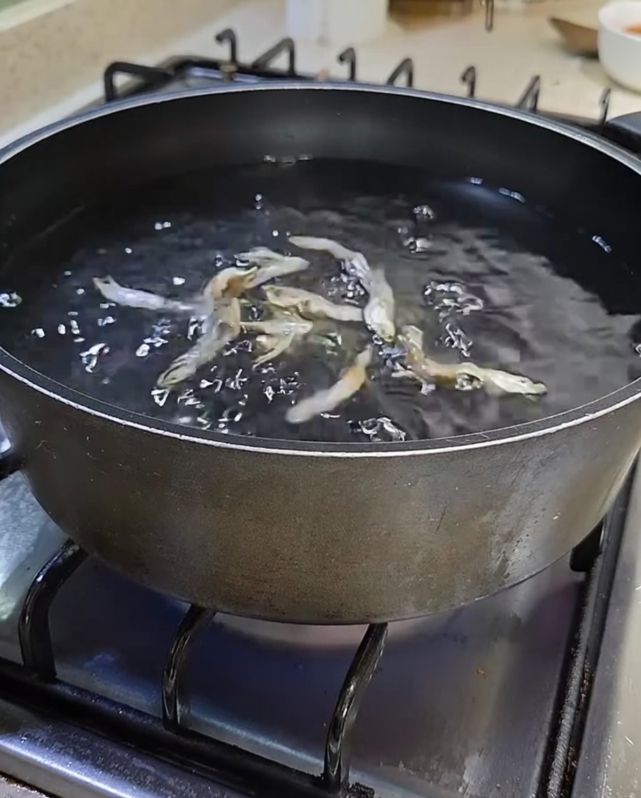 Una pentola nera su un fornello riempita dacqua e acciughe argentate essiccate.