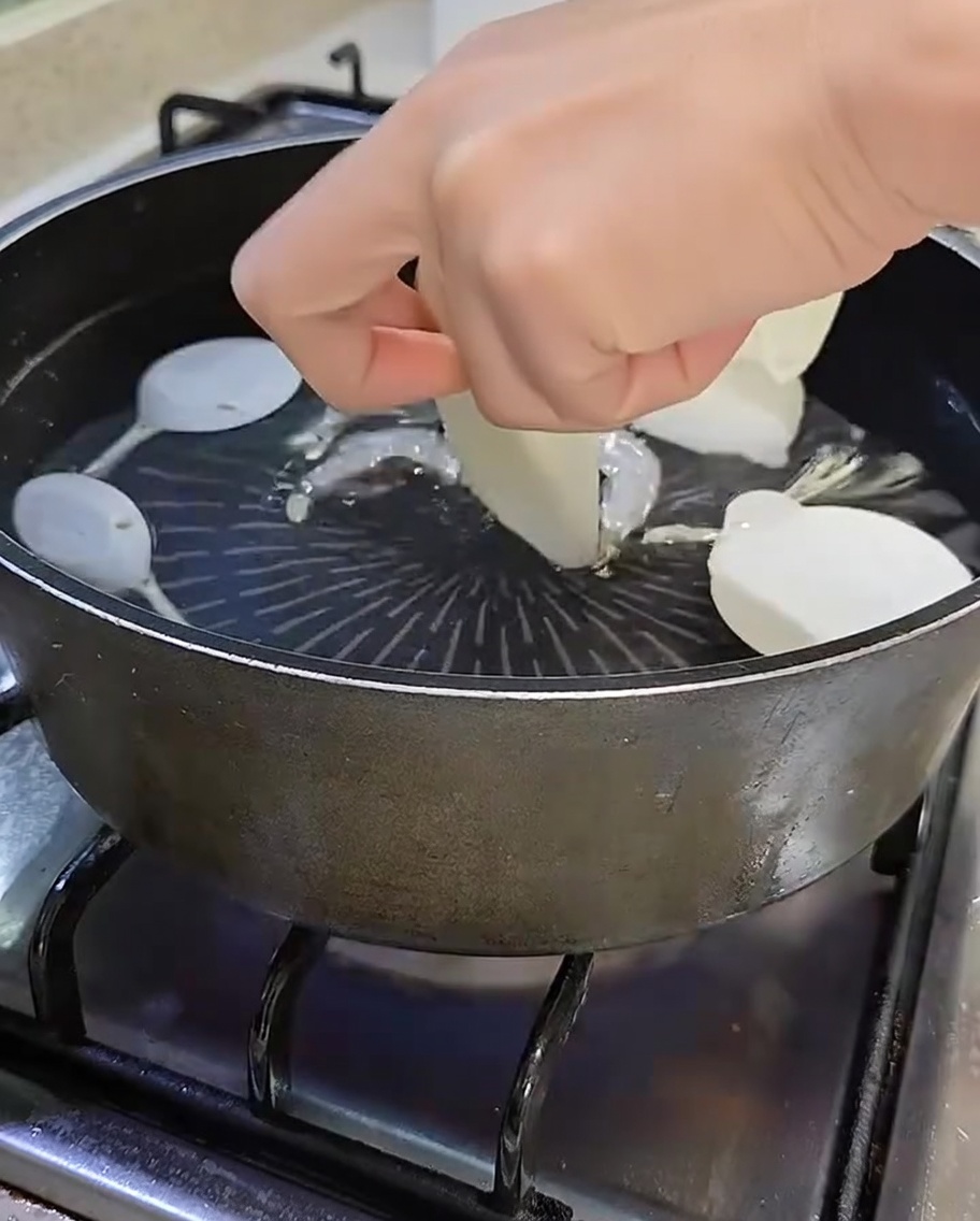 Pentola contenente acqua bollente, acciughe, shiitake, ravanello affettato e cipollotti verdi.