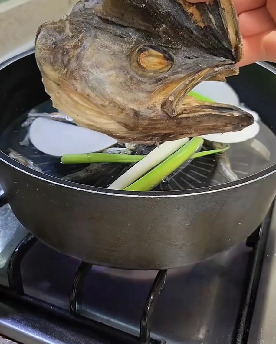 Una testa di pesce pollack essiccata tenuta sopra la pentola prima di essere aggiunta al brodo.