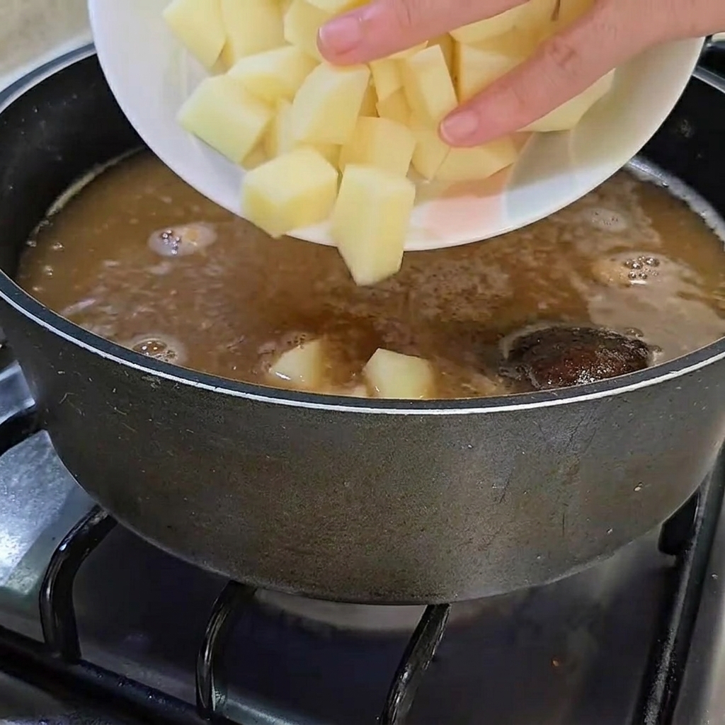 Patate crude appena tagliate a cubetti aggiunte alla pentola di brodo in ebollizione.