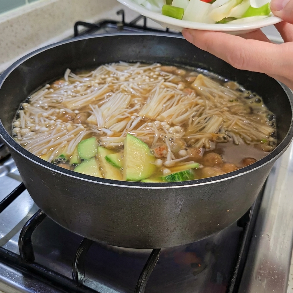 Cipolle tritate, cipollotti e peperoncini rossi e verdi aggiunti allo stufato, che contiene anche tofu a fette.