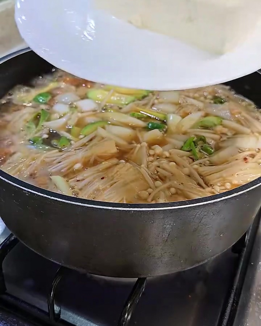 Fette di tofu bianco trasferite con cura da un piatto bianco nello stufato di pasta di soia bollente.