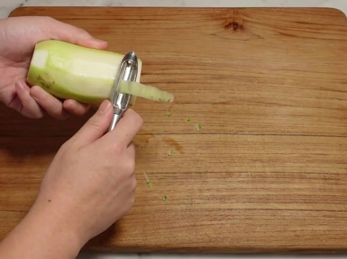 Un ravanello bianco crudo (daikon) viene sbucciato su un tagliere di legno.