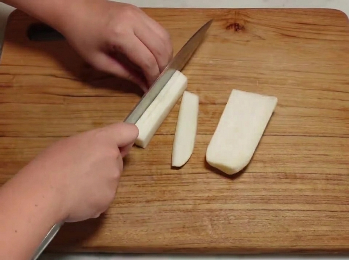 Daikon pelato tagliato a piccoli cubetti su un tagliere di legno.