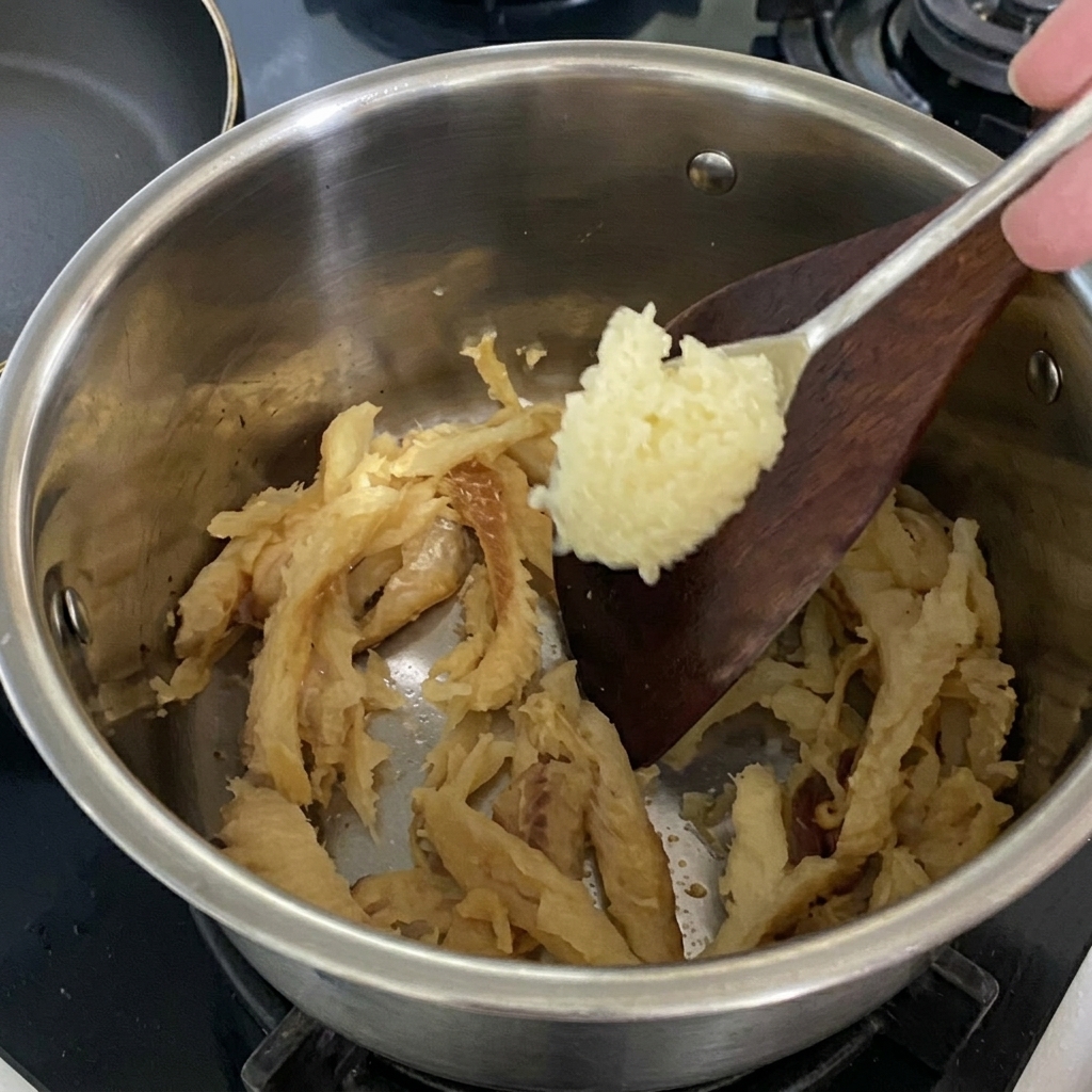 Un cucchiaio di aglio tritato aggiunto al pollack che sta rosolando nella pentola.