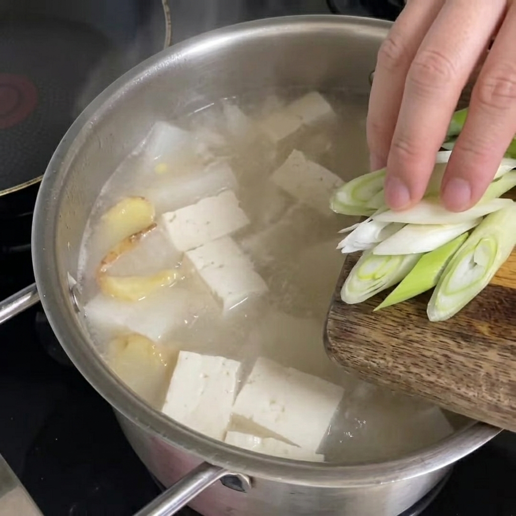 Cipollotti freschi tritati sparsi sulla zuppa di pollack bollente.