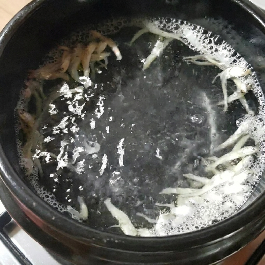 Un pentolino di pietra nera contenente acqua, acciughe essiccate e alga kelp, che bolle sul fornello.