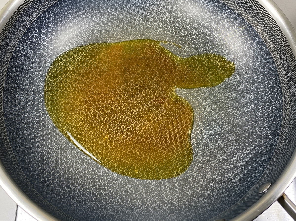 Un pezzo di strutto solido che si scioglie in olio caldo dentro un wok scuro.