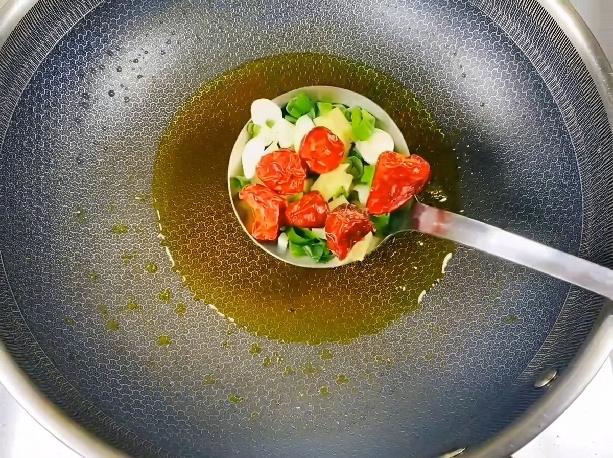 Cipollotti tritati, aglio e peperoncini secchi soffritti nel wok.