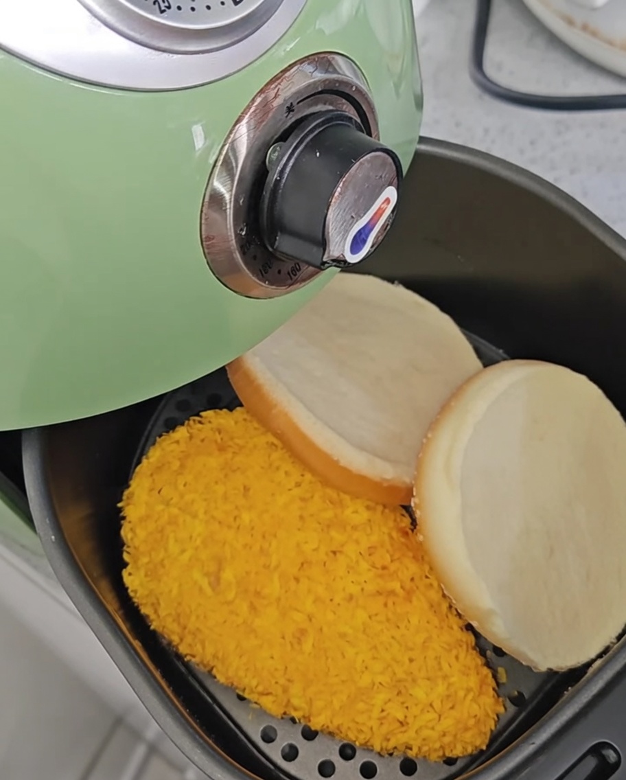 Filetti di pollo nella friggitrice dopo essere stati girati, con le metà del pane per burger posizionate accanto.