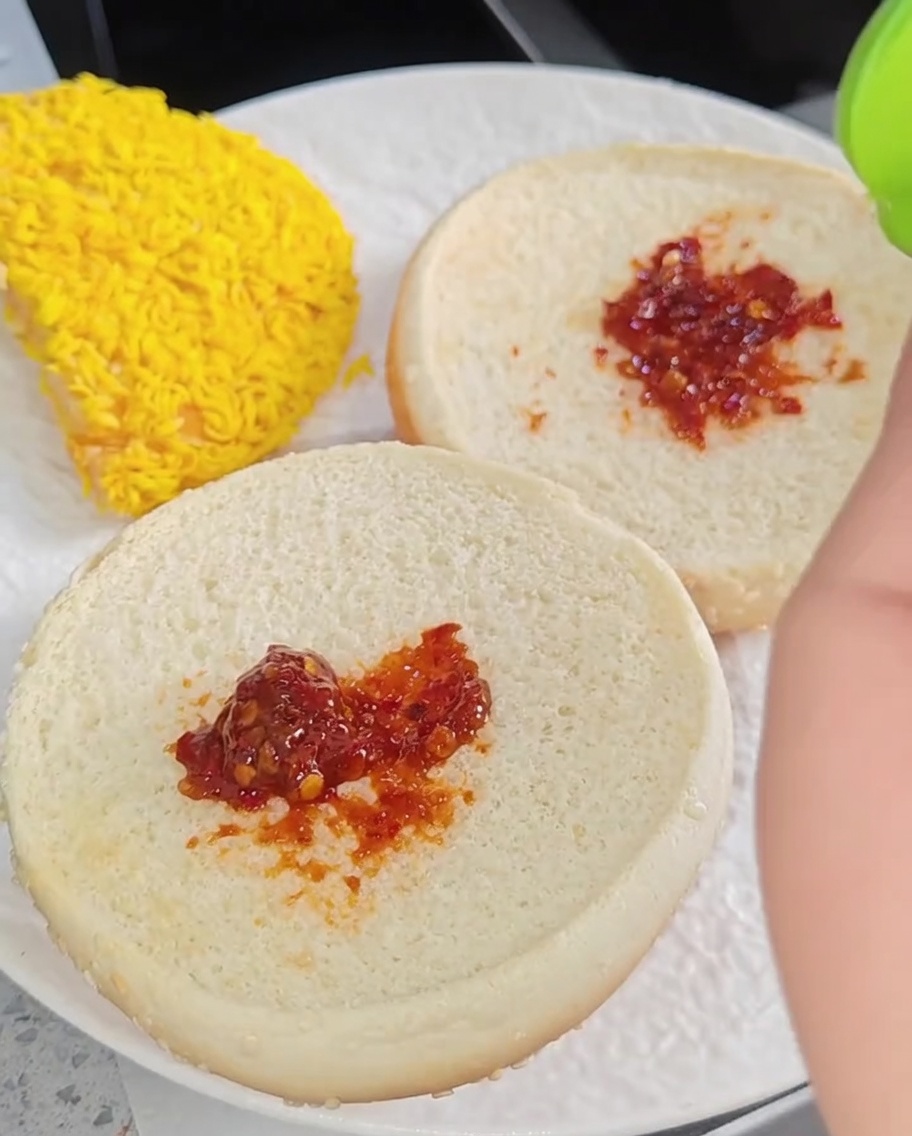 Un burger di pollo completo su un piatto, con strati di lattuga, due filetti di pollo, formaggio e una fetta di pomodoro.