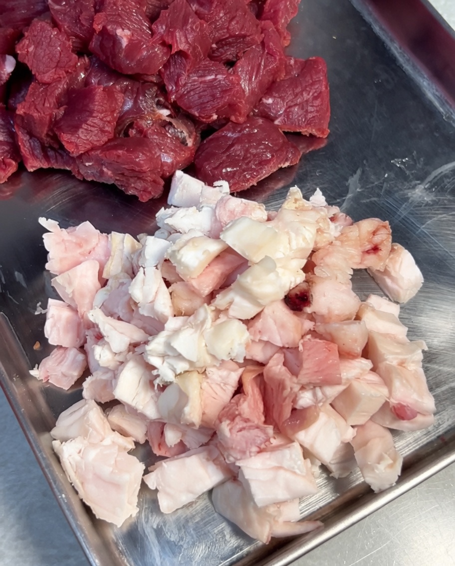 Pezzi di carne e grasso conditi con sale e pepe nero in una ciotola di acciaio inox.