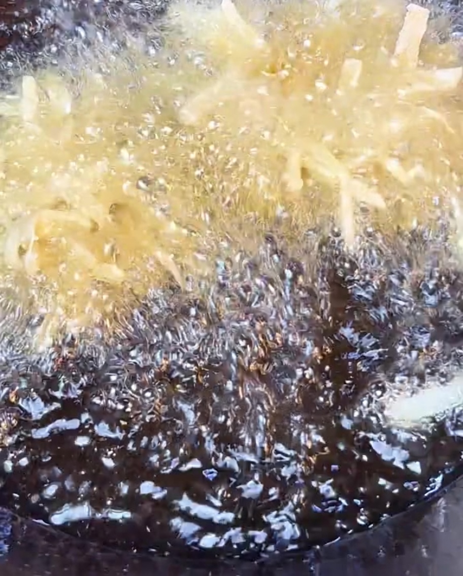 Patate sminuzzate croccanti che friggono in olio caldo fino a doratura.
