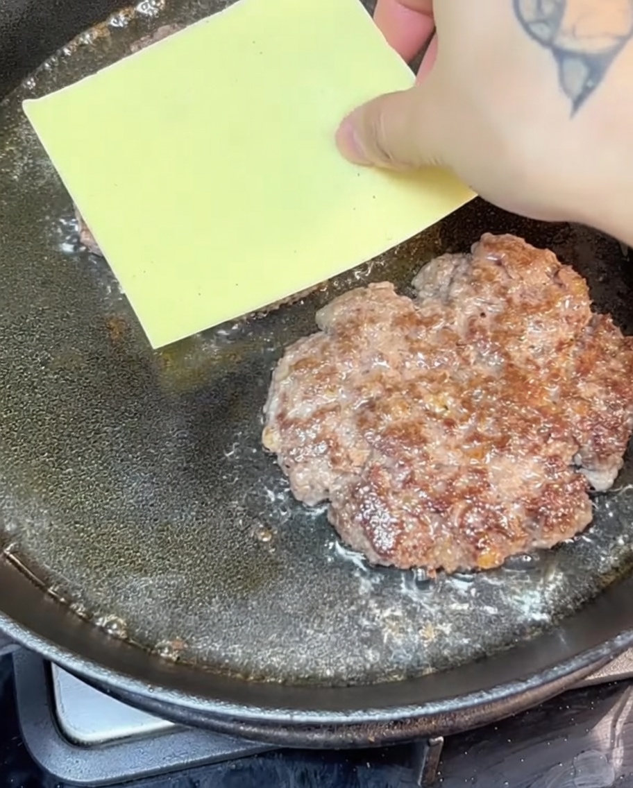 Burger di manzo con formaggio che sfrigola in una padella di ghisa.