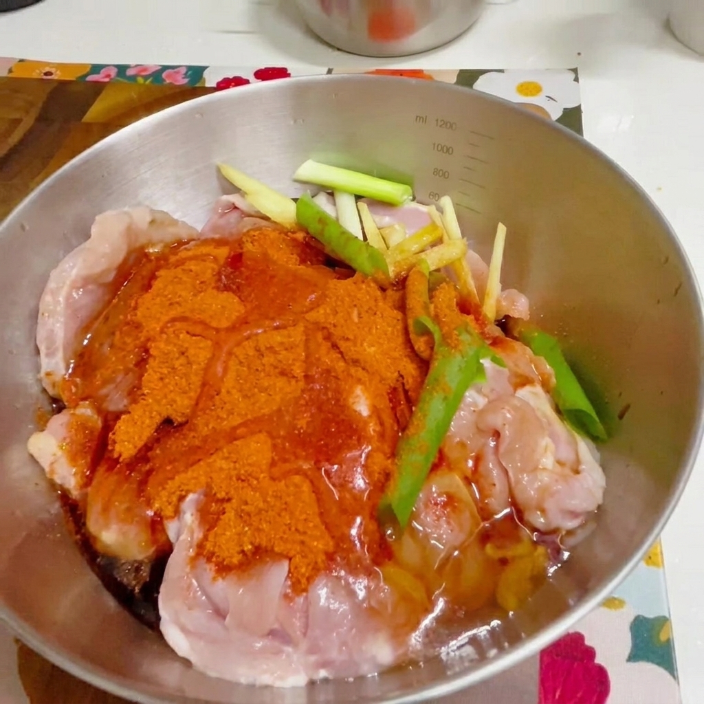 Una mano guantata che mescola il pollo condito in una ciotola di metallo.