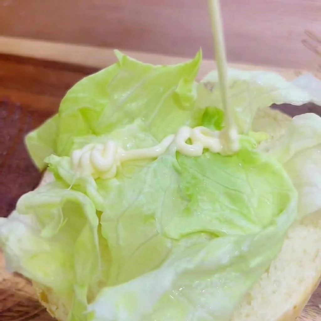 Maionese bianca spremuta a zig-zag sulla lattuga fresca sopra il panino.