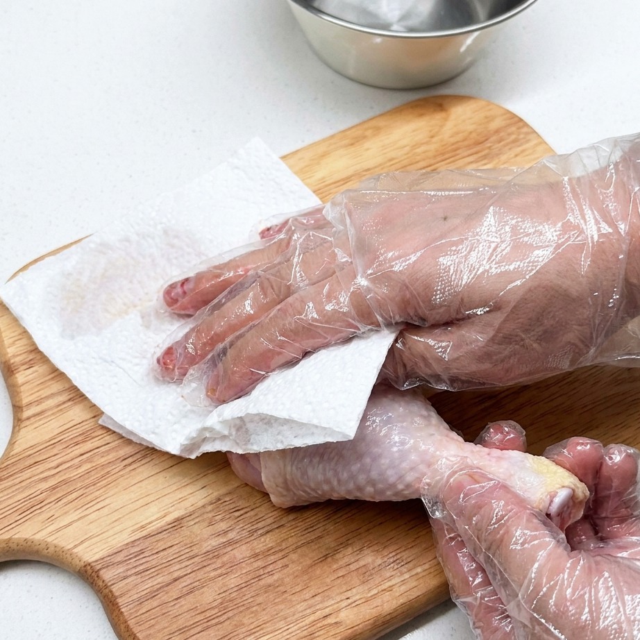 Coscia di pollo cruda su un tagliere di legno con carta assorbente.