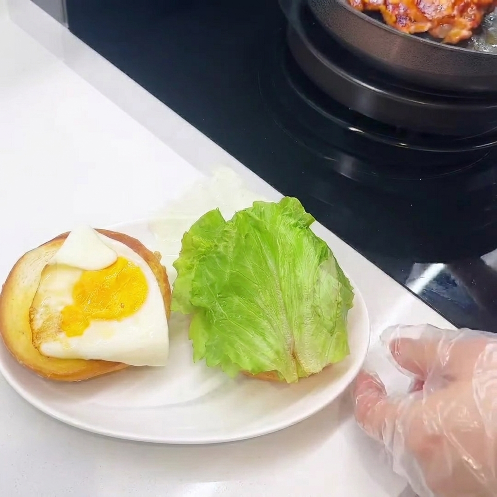 Primo piano dellassemblaggio del burger, con pollo, formaggio, uovo e lattuga impilati sul pane.