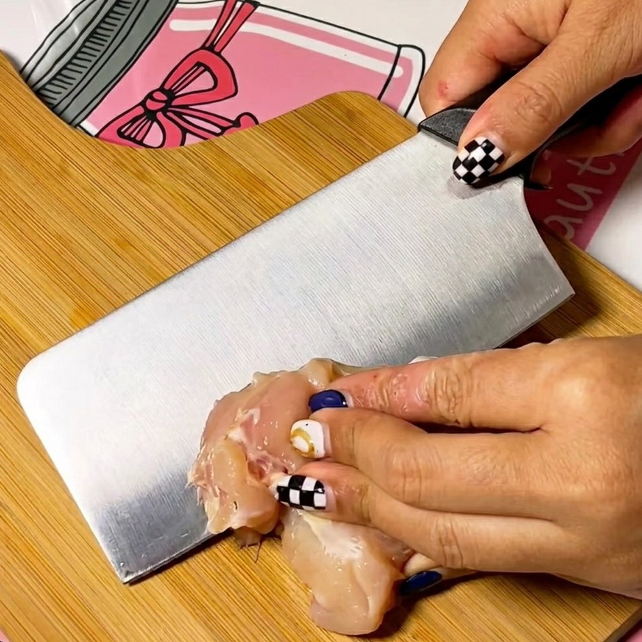 Sottili fette di petto di pollo crudo disposte con cura su un tagliere di legno pulito.