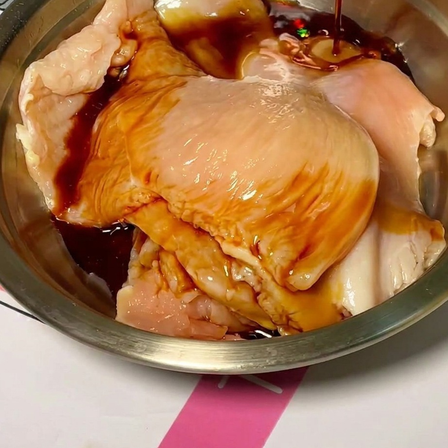 Fette di pollo crudo in una ciotola mentre vengono ricoperte da una marinata scura e saporita.