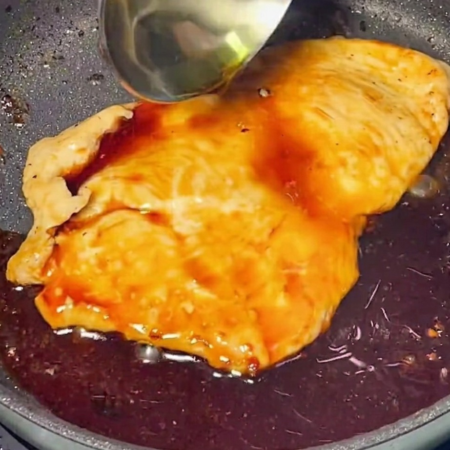 Una ricca e lucida salsa teriyaki versata sopra il pollo dorato in una padella.