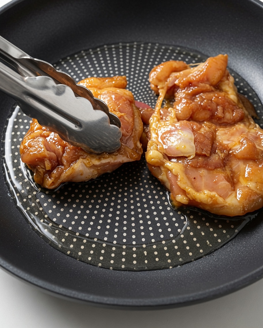 Sovracosce di pollo crude e marinate adagiate in una padella calda e oliata usando delle pinze di metallo.