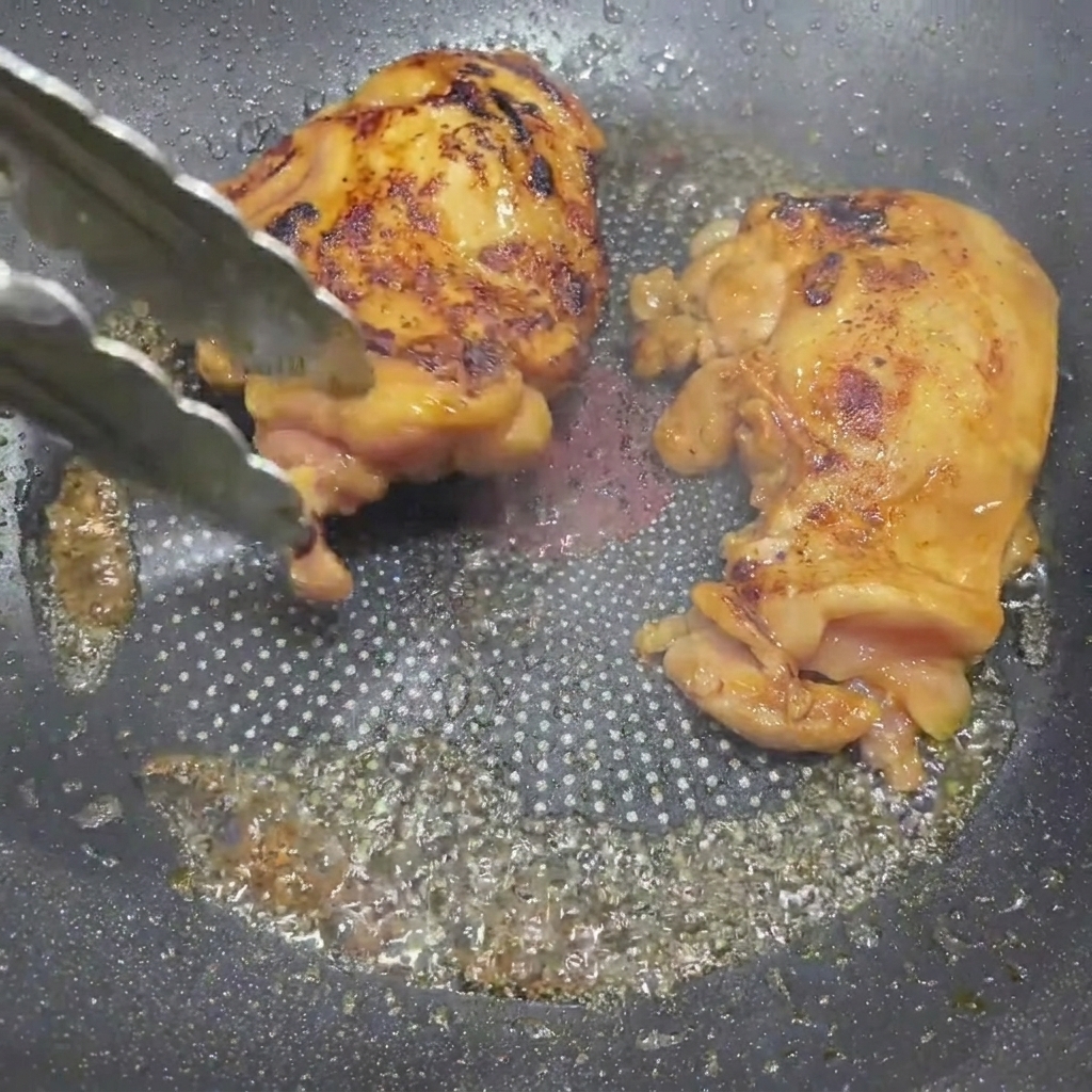 Sovracosce di pollo glassate alla teriyaki girate in padella con delle pinze da cucina.