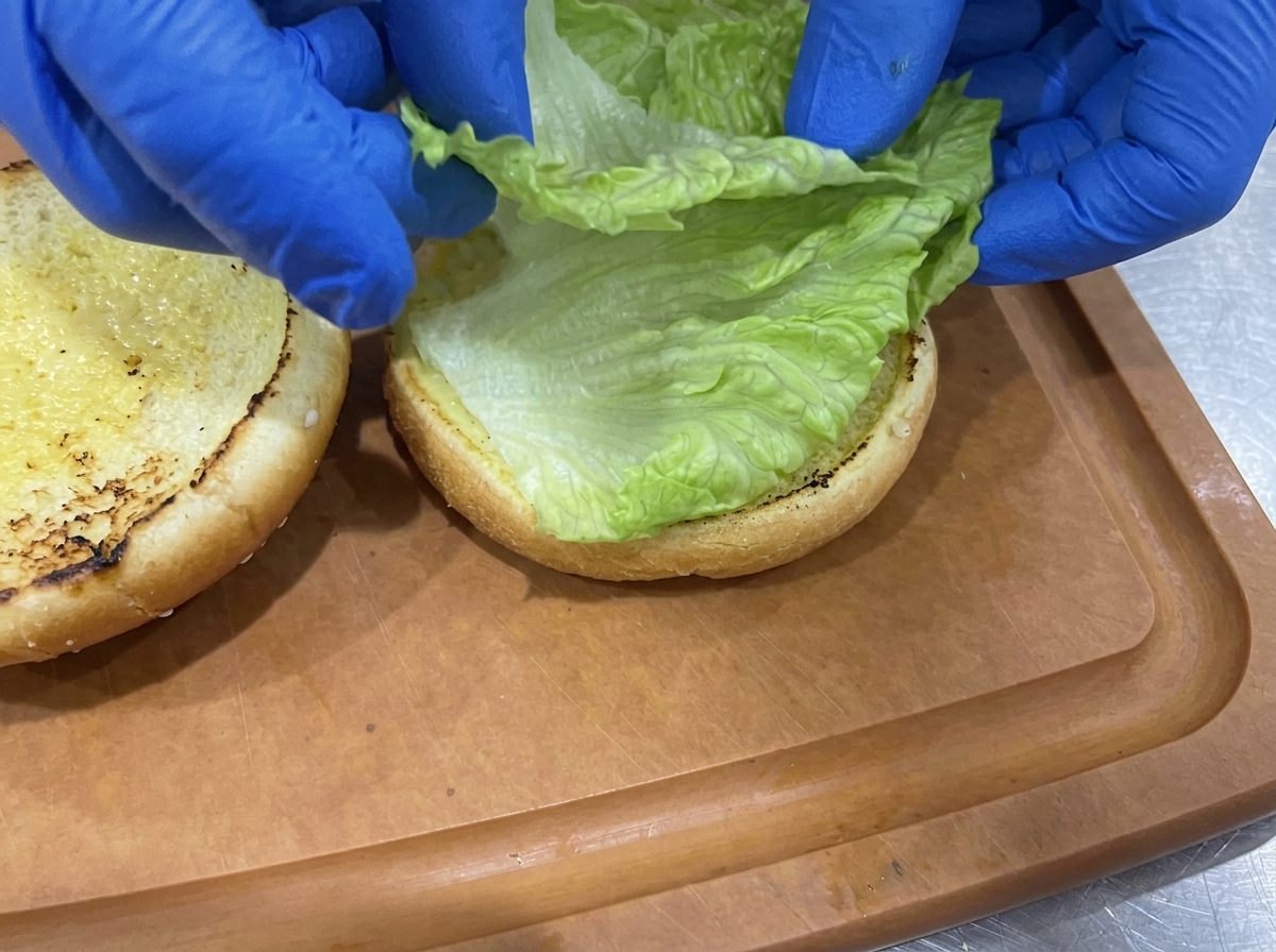 Foglie di lattuga verde e croccante disposte sulla metà inferiore tostata del panino.