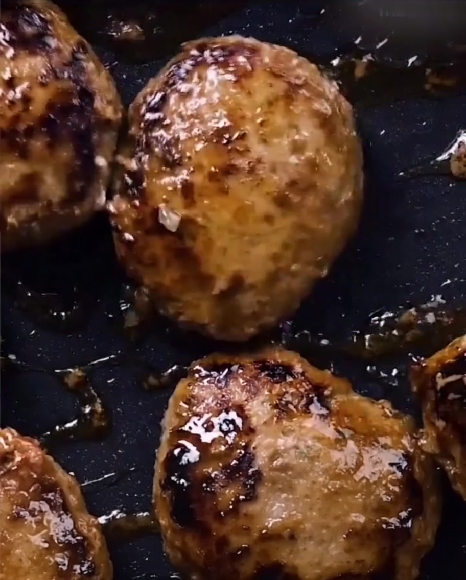 Hamburger steak che brillano con una glassa teriyaki scura e densa in padella.