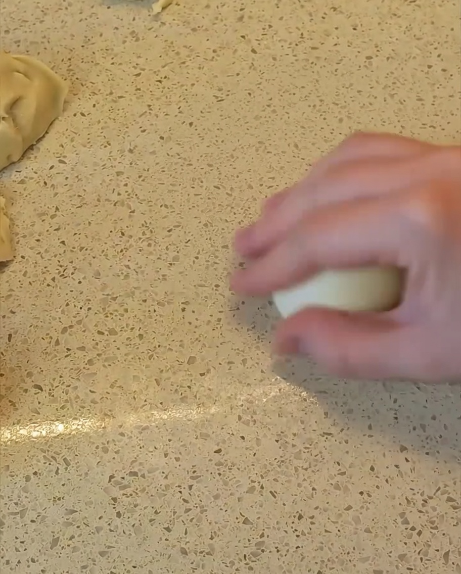 Una mano che fa roteare un pezzo di impasto sul piano di lavoro per formare una palla liscia e rotonda.