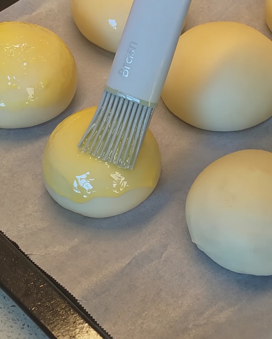 Un pennello in silicone applica il tuorlo duovo sulla parte superiore dei panini prima di cospargerli con i semi di sesamo.