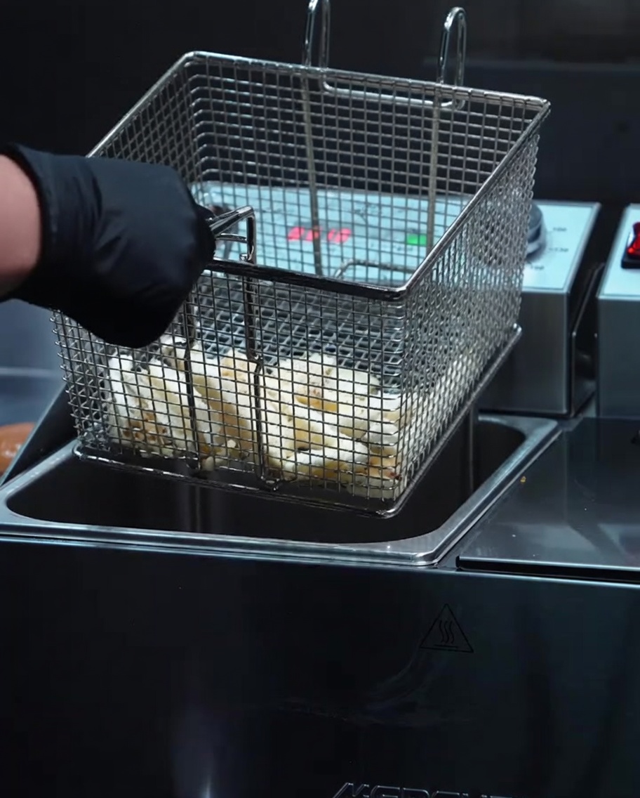 Patatine fritte dorate e croccanti appena sollevate dalla friggitrice in un cestello di metallo.