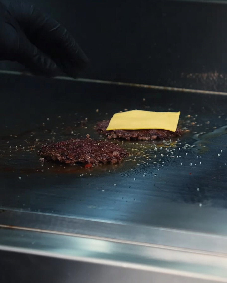 Fette di formaggio cheddar che si sciolgono sugli hamburger di Wagyu su una griglia rovente.