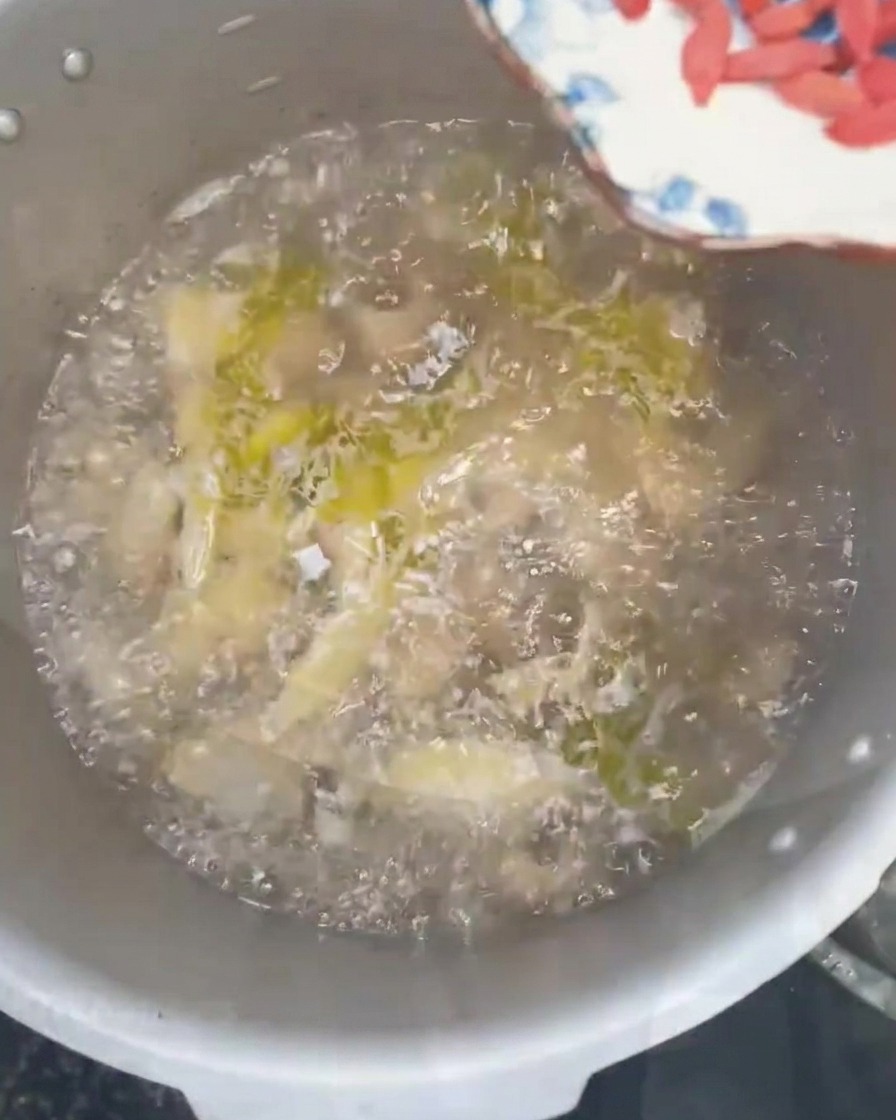 Bacche di goji e cipollotti freschi tritati sparsi in una pentola di zuppa di pollo bollente.