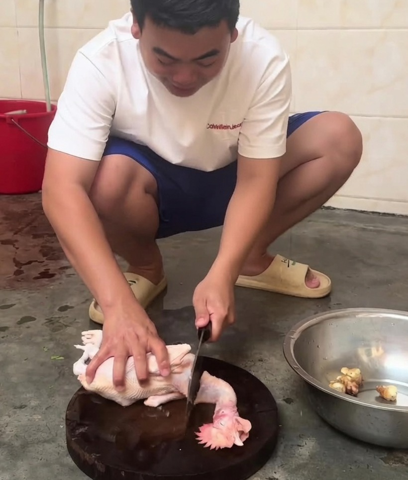 Un pollo intero crudo che viene tagliato in pezzi più piccoli con una mannaia su un tagliere di legno.