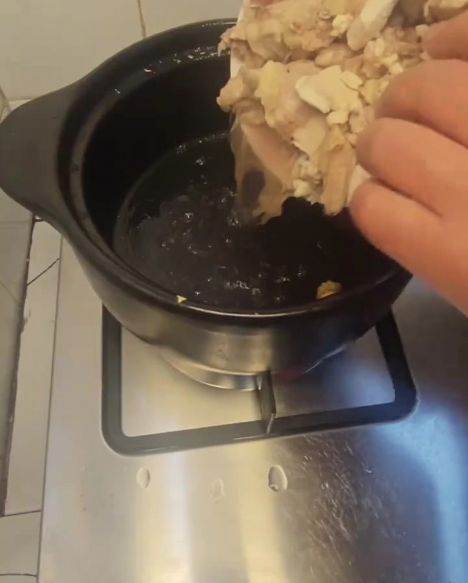 Pezzi di pollo sbollentati trasferiti da un piatto bianco in una pentola di coccio scura preriscaldata.