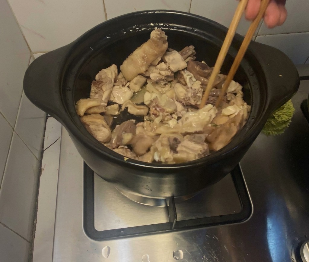 Pezzi di pollo rosolati con bacchette di legno allinterno di una pentola di coccio nera.
