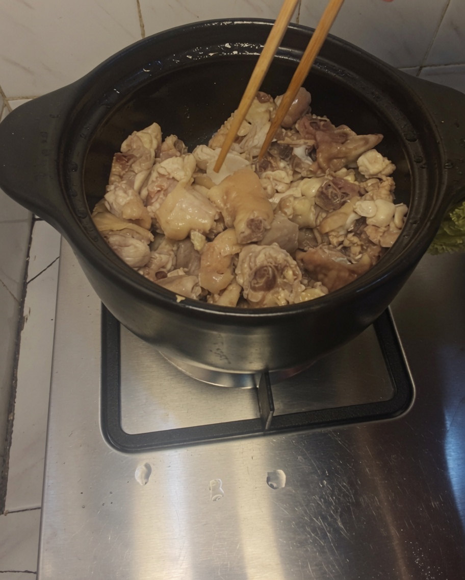 Bacchette di legno che mescolano pezzi di pollo e fette di zenzero in una pentola di coccio.