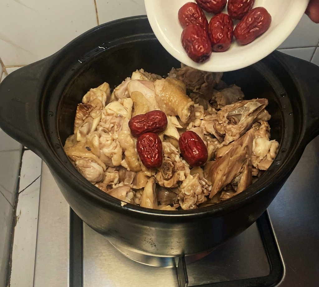 Un piattino bianco versa datteri rossi essiccati in una pentola di coccio con pollo.