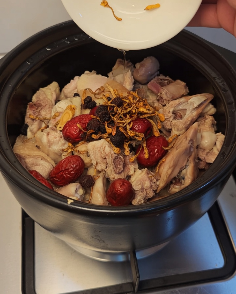 Fiori di cordyceps, bacche di goji scure e longan aggiunti al pollo e ai datteri nella pentola.