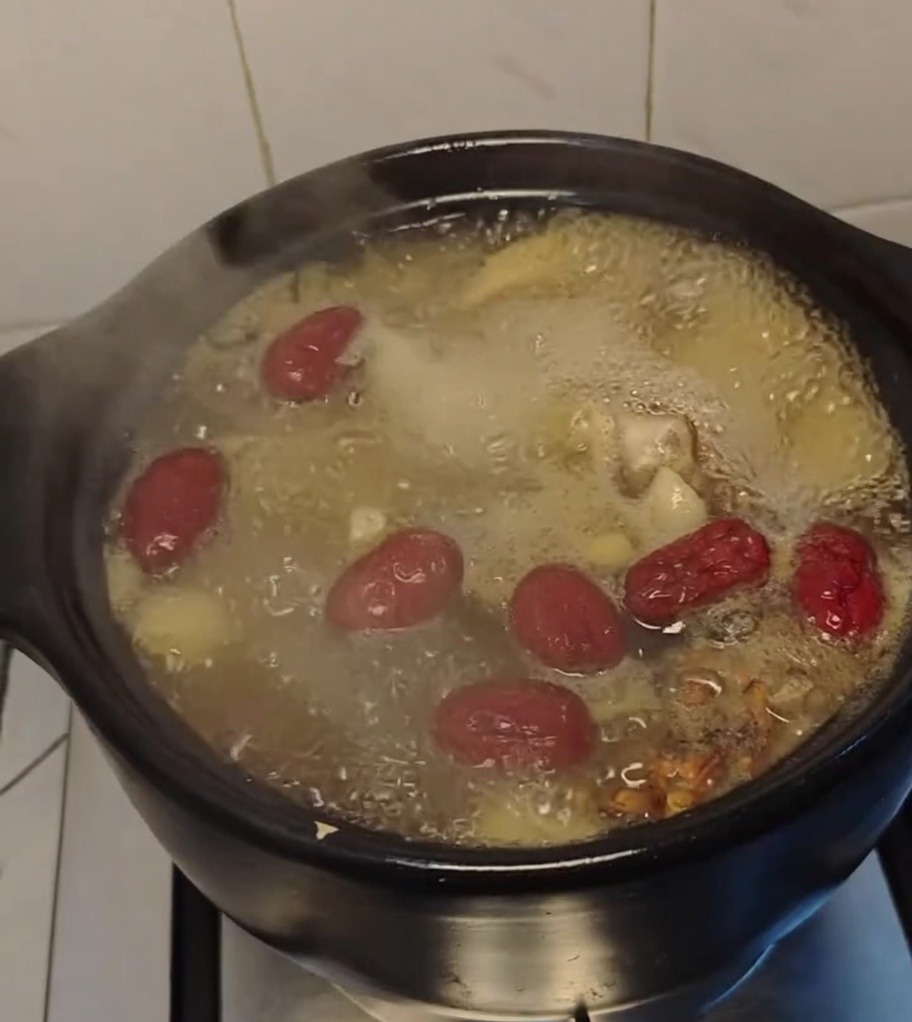 Zuppa di pollo che sobbolle in una pentola di coccio con datteri rossi in superficie.
