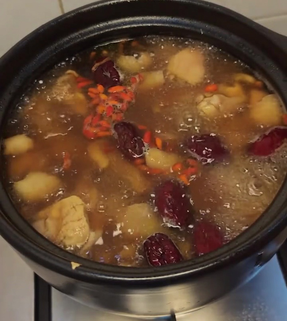 Zuppa di pollo che bolle guarnita con bacche di goji vibranti e datteri rossi.