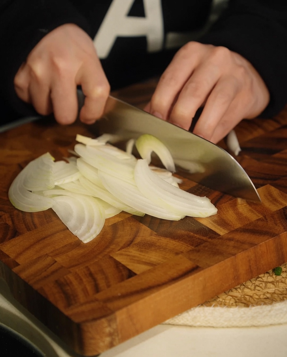 Strisce di cipolla bianca tagliate sottilmente su un tagliere di legno.