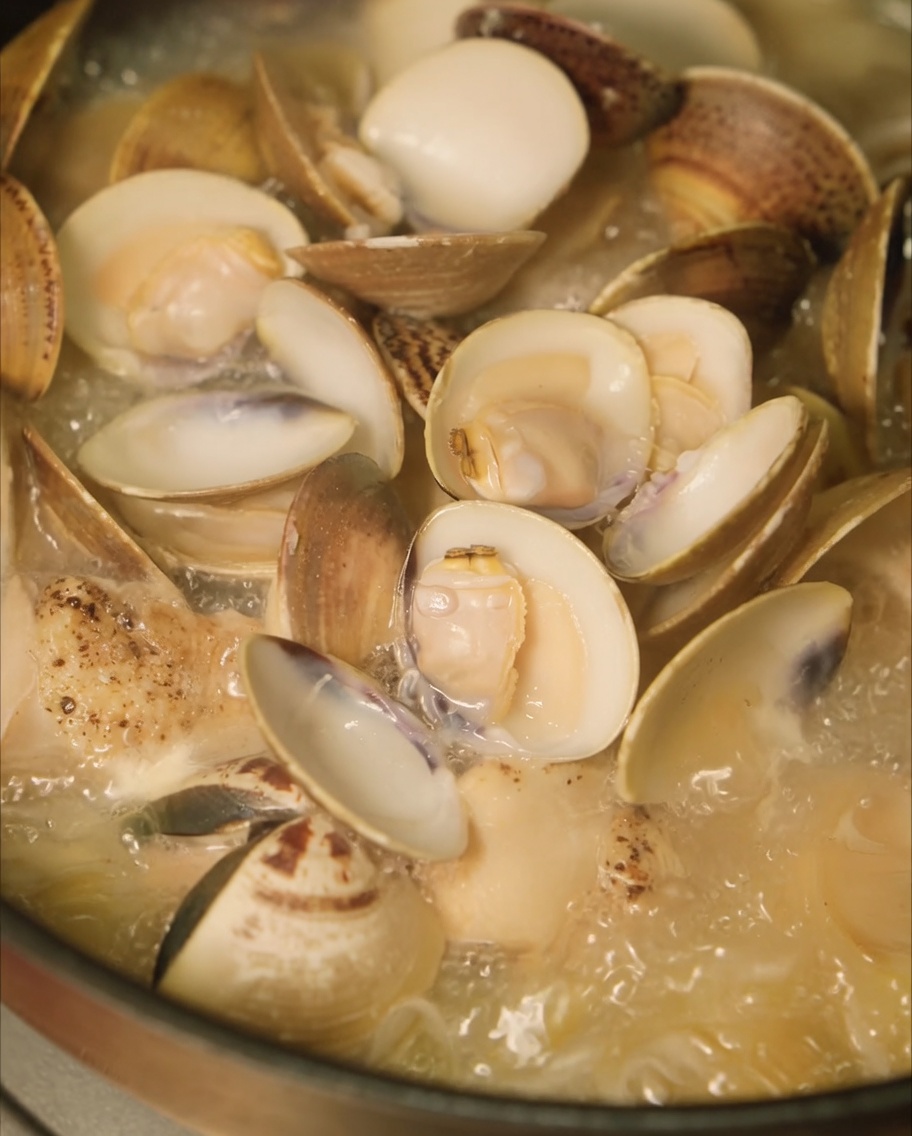 Vongole fresche aggiunte alla pentola con la zuppa di pollo e cipolle per la cottura a vapore.