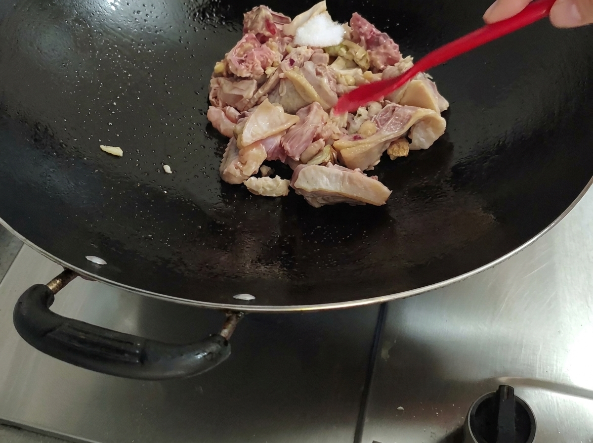 Aggiunta del sale al pollo nel wok utilizzando una spatola rossa.