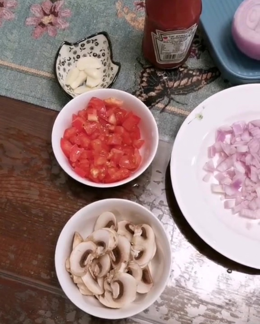 Una ciotola con pomodori freschi tagliati, funghi a fette e aglio tritato su un tavolo.