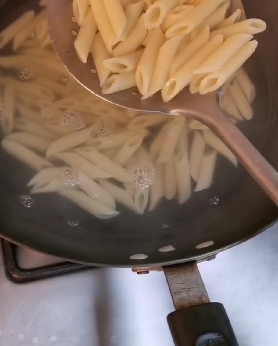 Penne sollevate dallacqua bollente con un grande cucchiaio forato.
