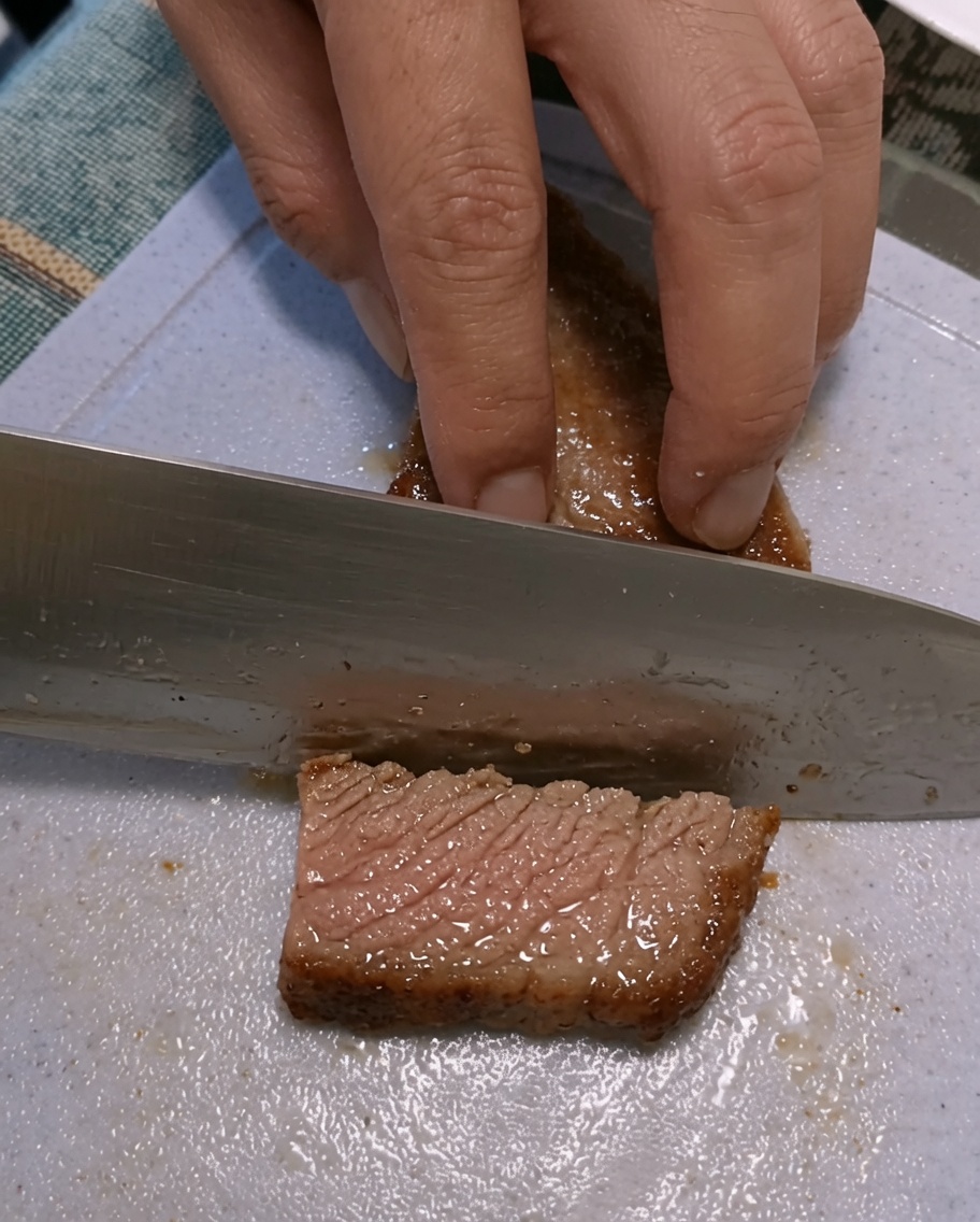 Mani che affettano una bistecca rosolata su un tagliere di plastica.