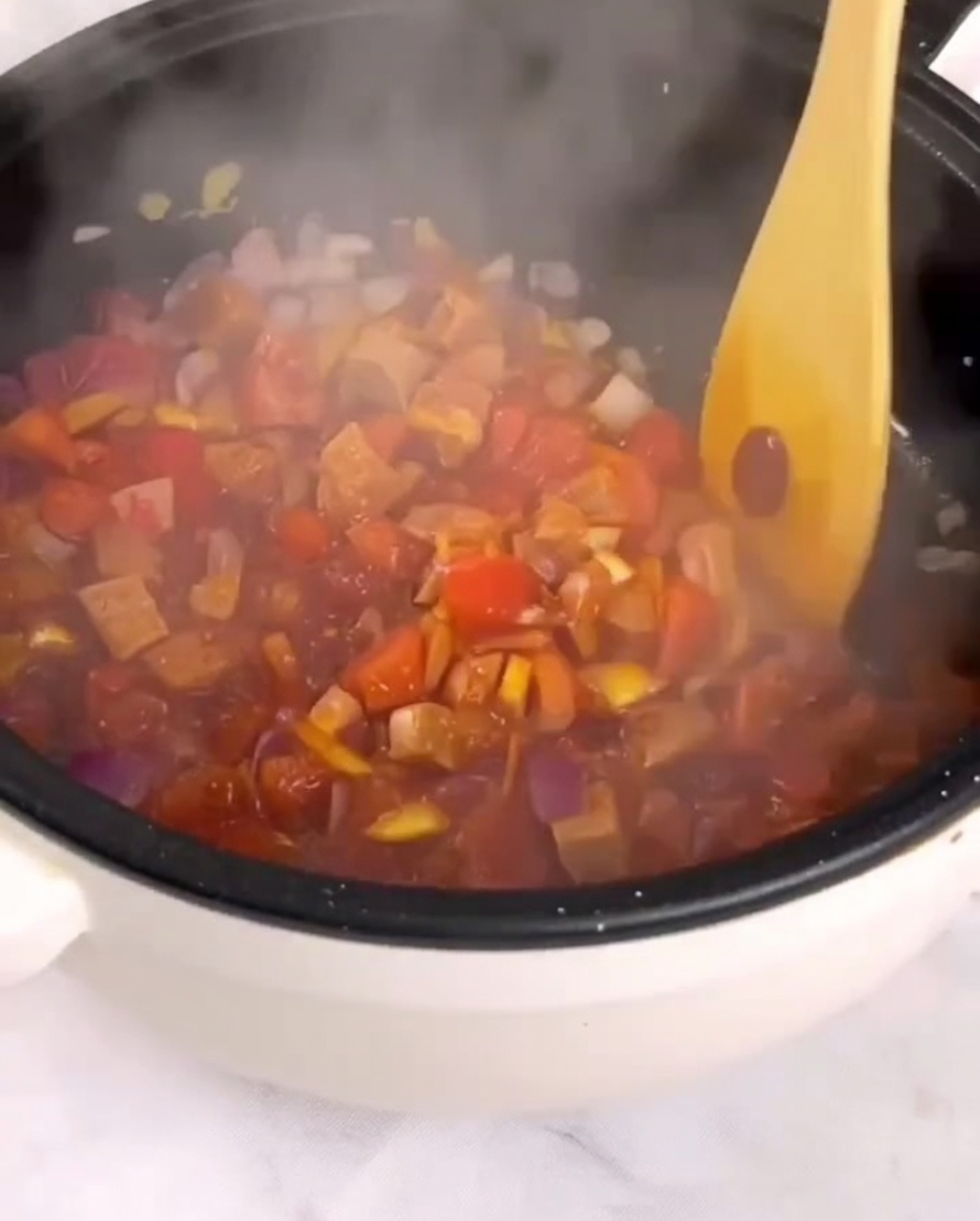 Pomodori a dadini, prosciutto e verdure saltati in padella con una spatola di legno.